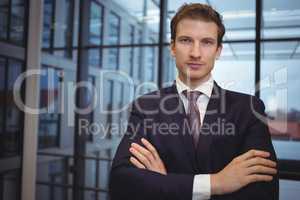 Portrait of handsome businessman standing with arms crossed in corridor