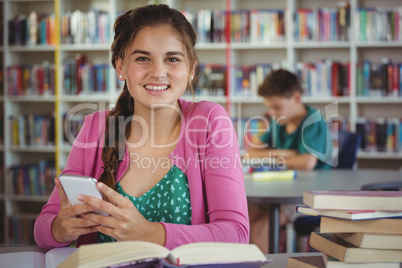 Smiling schoolgirl using mobile phone in library at school