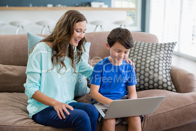 Smiling mother and son sitting on sofa using laptop in living room