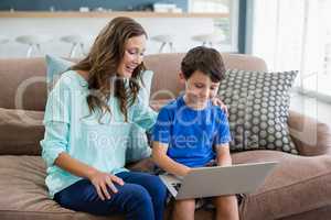 Smiling mother and son sitting on sofa using laptop in living room