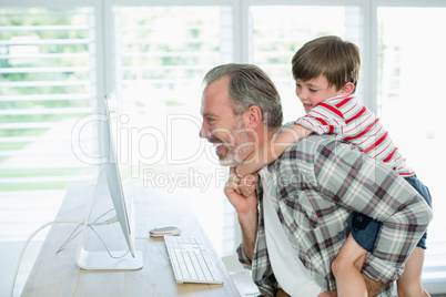Playful father and son working on computer at home