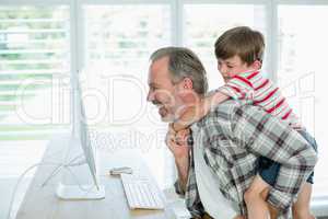 Playful father and son working on computer at home
