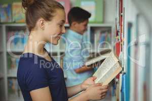 Smiling schoolgirl reading book in library