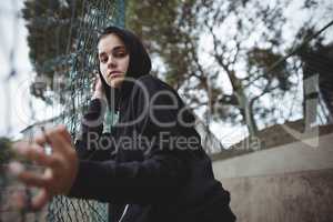 Anxious teenage girl leaning on wire mesh fence at school campus