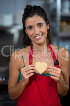 Portrait of smiling female staff showing heart shape cookie at counter