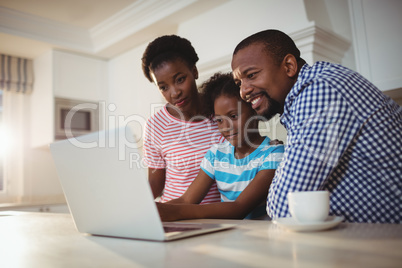 Parents and daughter using laptop in kitchen