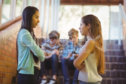 Two schoolgirls with arms crossed standing face to face in corridor