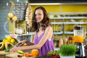 Smiling shop assistant chopping leaf vegetable at counter