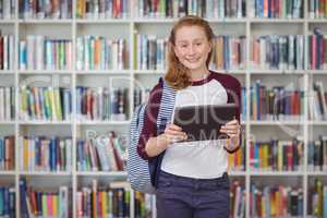 Portrait of happy schoolgirl holding digital tablet in library