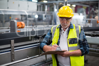 Male factory worker maintaining record on clipboard