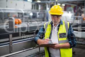 Male factory worker maintaining record on clipboard