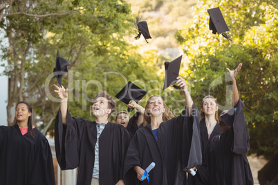 Successful graduate school kids throwing mortarboard in air in campus