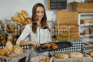 Portrait of smiling female staff placing croissant on tray at counter
