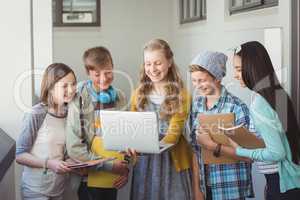 Smiling school students using laptop in corridor