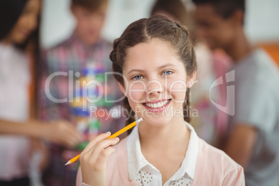 Portrait of smiling schoolgirl standing with pencil in classroom