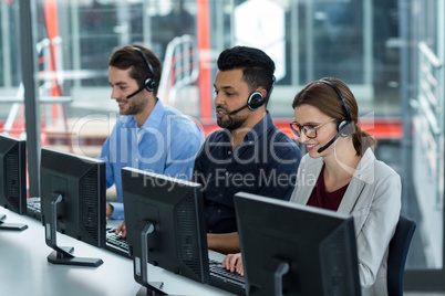 Business executives with headsets using computers at desk in office