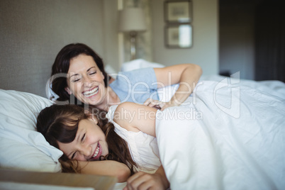 Mother and daughter laughing in bed