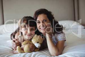 Mother and daughter lying on bed with teddy bear in bedroom