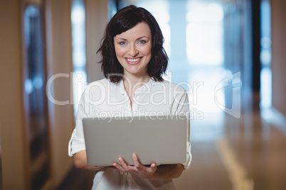 Portrait of female business executive using laptop in corridor