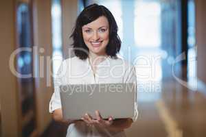 Portrait of female business executive using laptop in corridor