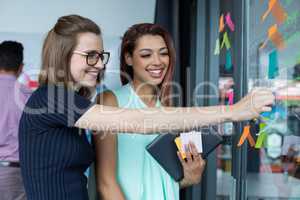 Smiling business executive sticking sticky note on glass