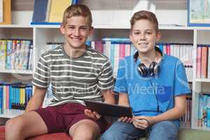 Portrait of happy schoolboys holding digital tablet in library