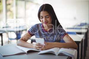 Schoolgirl using mobile phone while studying in classroom