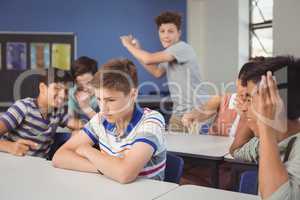 School friends bullying a sad boy in classroom