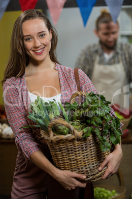 Smiling woman holding basket of green leafy vegetables in the grocery store