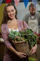 Smiling woman holding basket of green leafy vegetables in the grocery store