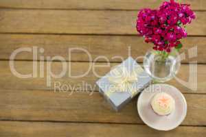 Gift box and flower vase with cupcake in plate on wooden plank