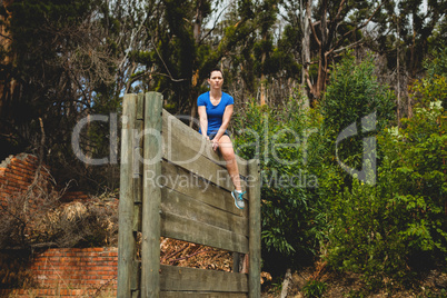 Fit woman sitting over wooden wall obstacle