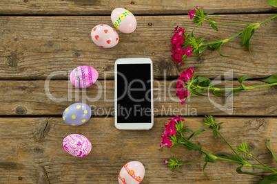 Painted Easter eggs, flowers and mobile phone on wooden surface