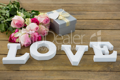 Gift box with bunch of roses and love alphabet on wooden plank