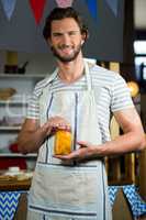 Smiling shop assistant holding a jar of pickle