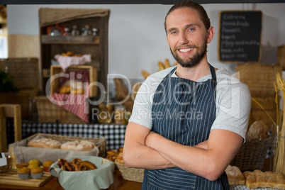 Portrait of smiling male staff standing with arms crossed at counter