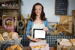 Portrait of smiling staff showing digital tablet at bakery counter
