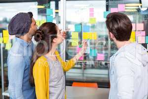 Executives discussing over sticky note on glass wall