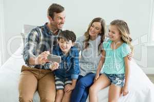 Smiling man taking selfie with family while sitting in bedroom