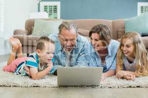 Smiling family using laptop while lying on carpet in living room