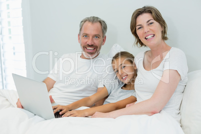 Smiling family using laptop on bed in bedroom at home