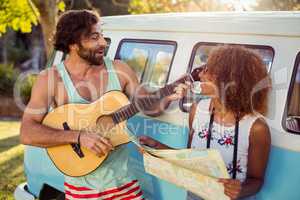 Man playing guitar near campervan and woman holding map beside him