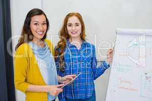 Portrait of smiling colleagues discussing over digital tablet and flip chart in conference room