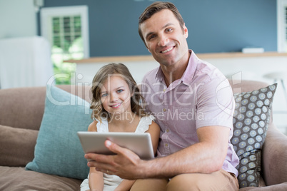 Father and daughter sitting on sofa using digital tablet in living room at home