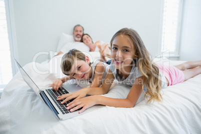 Smiling girl and boy using laptop on bed in bedroom at home