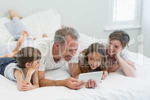 Smiling family using digital tablet while lying on bed in bedroom