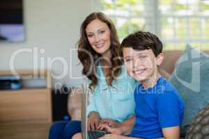 Portrait of smiling mother and son sitting on sofa using laptop