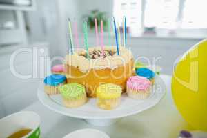 Close up of birthday cake on stand with cup cake and candles
