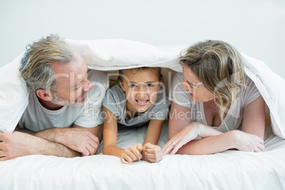 Happy family lying under blanket on bed at home