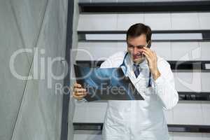 Male doctor discussing x-ray on mobile phone while walking downstairs